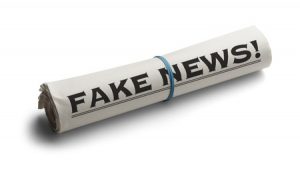 69458633 - rolled up newspaper with headline of fake news isolated on white background.